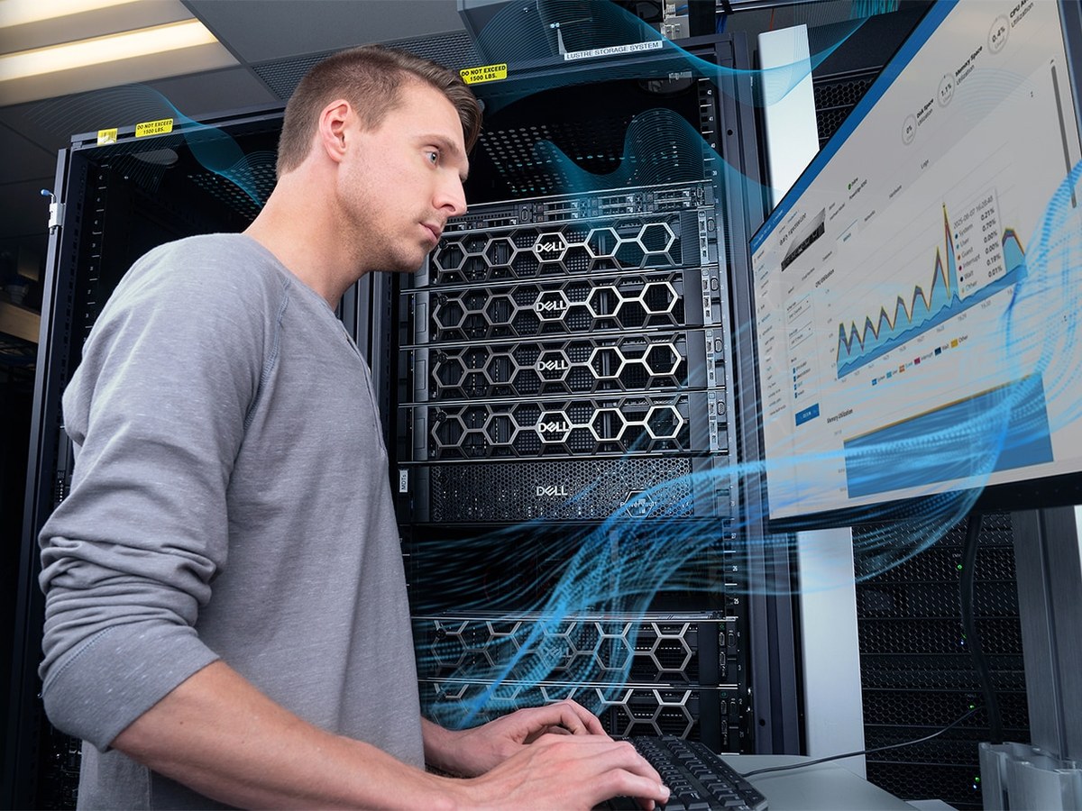 Người đàn ông áo xám kiểm tra dữ liệu trên màn hình cạnh tủ server DELL đen-bạc trong trung tâm dữ liệu.