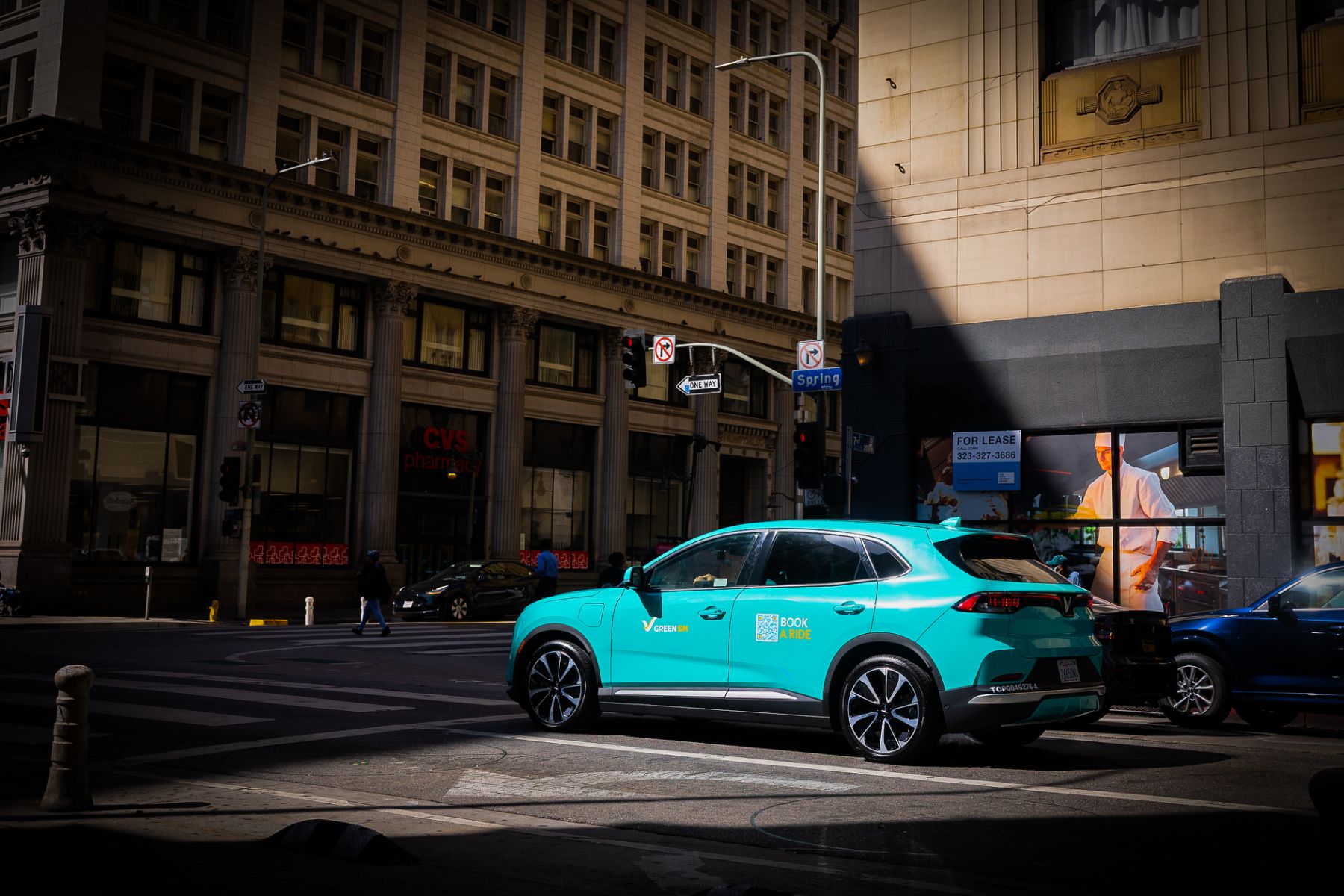 Xe taxi điện VinFast VF 8 màu xanh cyan của Green SM qua ngã tư đường Spring tại Los Angeles
